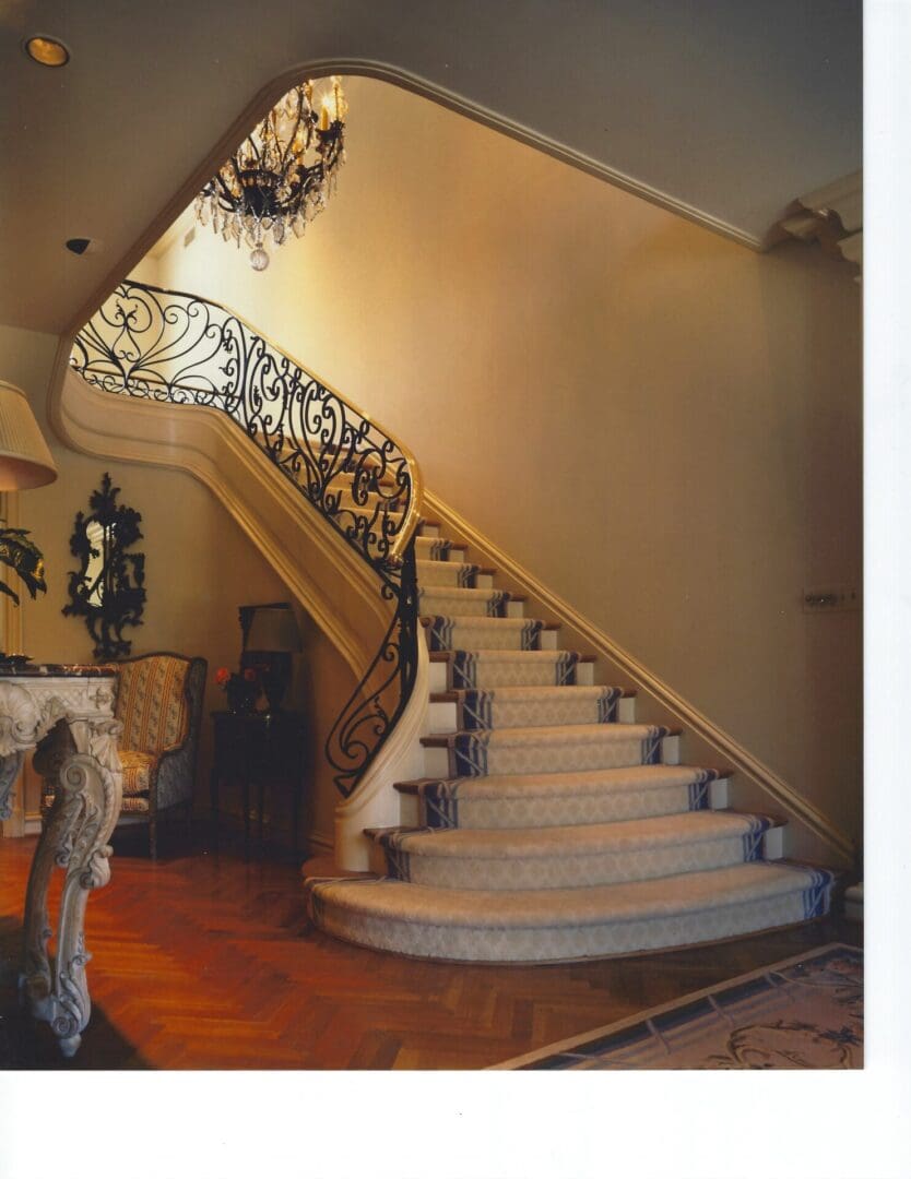 Elegant staircase with ornate railing and chandelier.